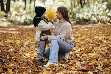 Mother with son having fun in autumnal park, playing with leaves