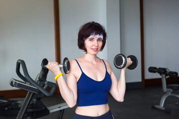 Fototapeta premium Sports woman lifting dumbbells in gym with large window.