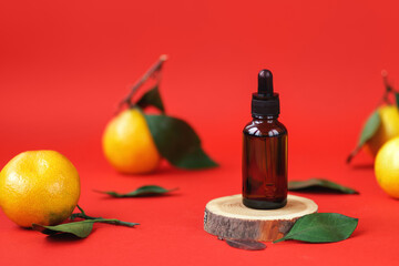 Face serum, essential oil in amber glass dropper bottle on wooden podium. Natural composition of beauty products on red background with fresh tangerines and lemons in soft focus. Anti-age moisturizer