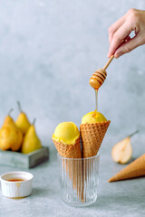 A woman's hand holding a wooden stick for honey, sweet honey falling on creamy ice cream with pear and ginger in waffle cone in a glass. Healthy vegan organic dessert.
