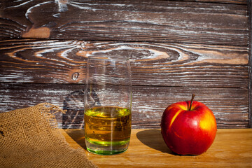 A glass of freshly squeezed apple juice and a red ripe apple on a table covered with a cloth...