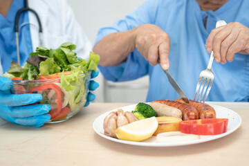 Asian senior or elderly old lady woman patient eating breakfast and vegetable healthy food with hope and happy while sitting and hungry on bed in hospital.