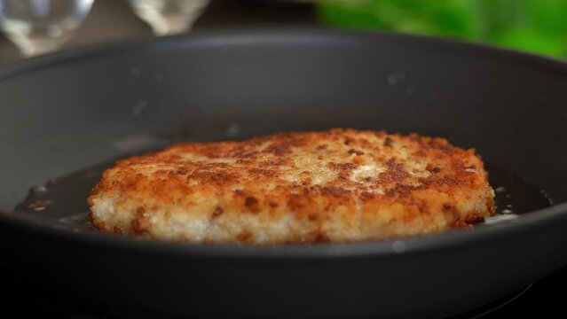 Camera movement on fried chicken schnitzel in sizzling oil in hot frying pan. Chicken meat is fried on stove. Food concept