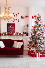 Interior of bright modern living room with fireplace, chandelier and comfortable sofa decorated with Christmas tree and red gifts