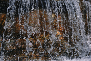 Close up of a water fall falling into a pond below creating a lot of water spray, bubbles and splashes