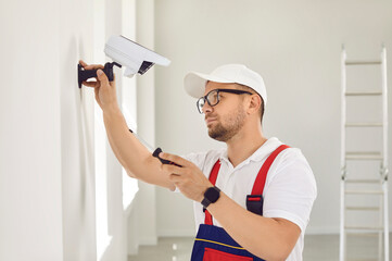 A Caucasian male repairman in uniform and glasses holds a screwdriver and installs video...