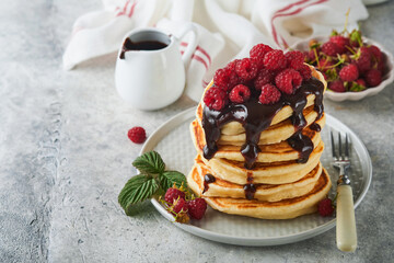 American pancakes. Stack pancakes with fresh raspberry with chocolate glaze or toppings in white bowl on light gray table background. Homemade classic american pancakes. Magazine concept. Top view.