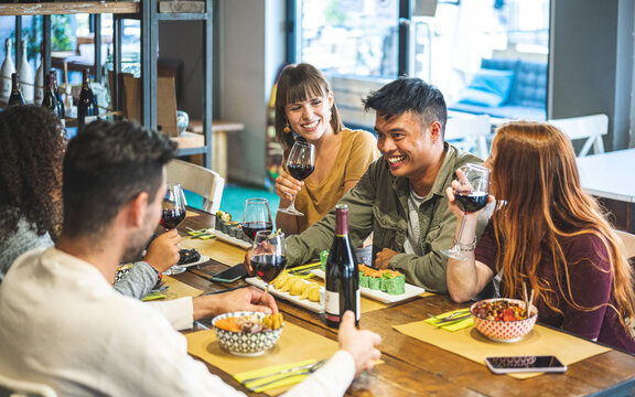 Young People Dining And Having Fun Drinking Red Wine Together At Restaurant, Happy Friends Eating Asian Food,  Millenials Life Style Concept, Muted Warm Indoor Filter