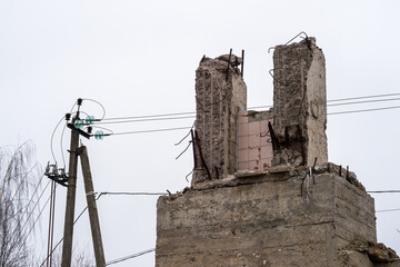 Concrete support close-up of a destroyed building against the background of power lines and gray sky. Background