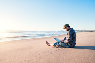 mature latin man sitting on the beach sand with his notebook working at sunset