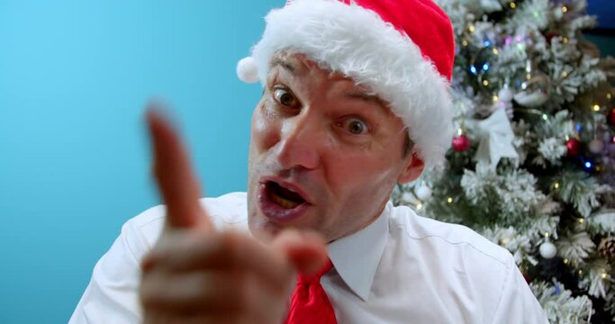 Portrait an upset middle-aged father in Christmas Santa hat.Man with an angry face rudely speaks to camera, waves his index finger and says something, looking at camera, his frustration, aggression