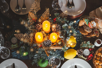 Fototapeta na wymiar Top view of beautiful decorated Christmas table with candles cookies wine glasses plates. Christmas eve night dinner table time to celebrate family gathering. New year party at home with happiness.