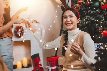 Group of happy Asian friends celebrating Christmas and decorate the Christmas tree indoors. Beauty woman with Christmas Gifts. New Year party. Woman hands decorate Christmas tree red ball, bauble.