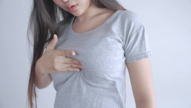 Asian woman wearing a gray T-shirt is self-checking for breast cancer at home.