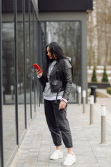 Beautiful caucasian woman with long dark hair talking by phone with friend while standing on street