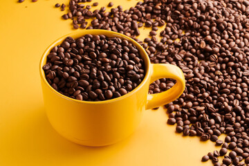 Cup of freshly brewed roasted coffee beans on yellow background