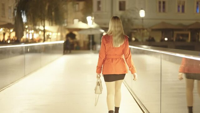 Blonde woman in red coat and mini skirt walk over bright bridge at night 4K
