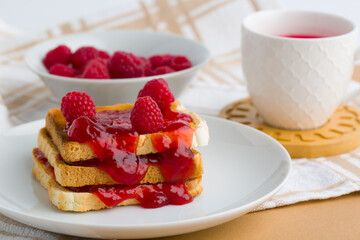 Toast with raspberry jam and cup of tea on beige table.