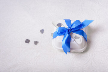 A bento cake box with a blue ribbon, candle and spoon on a white background