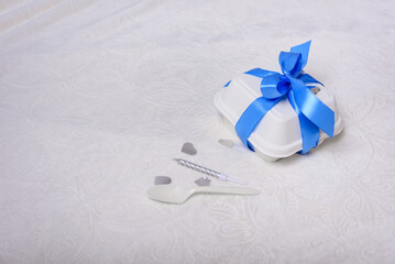A bento cake box with a blue ribbon, candle and spoon on a white background