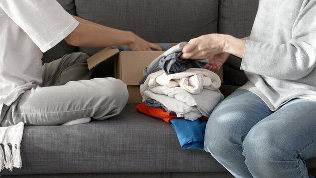 Woman and child sorting clothes and packing into cardboard box. Donations for charity, help low income families, declutter home, sell online, moving moving into new home, recycling, sustainable living