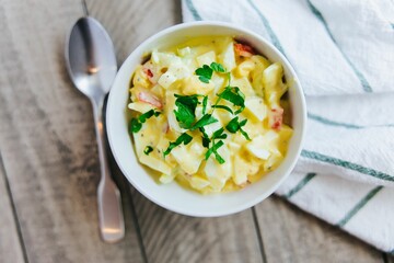 High angle of a potato salad inside a white plate with a spoon and a handkerchief on the table