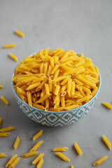 Homemade Raw Dry Mini Penne Pasta in a Bowl on a gray background, side view.