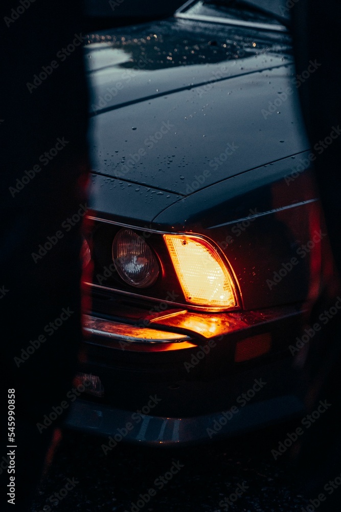 Sticker Vertical closeup of a car's headlight captured after rain, with water drops on the car