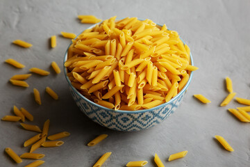 Homemade Raw Dry Mini Penne Pasta in a Bowl on a gray background, side view.