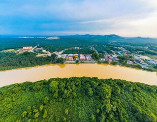 Aerial wide angle shot yellow river flowing through lush green forests and buildings in Malaysia