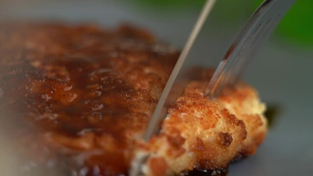 Close up of knife cuts fried chicken schnitzel with sauce on plate. Chicken breaded meat, steak. Food concept