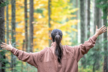 Woman on a blurred background of the autumn forest, view from the back.