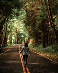 Vertical shot of a woman walking alone on a forest road