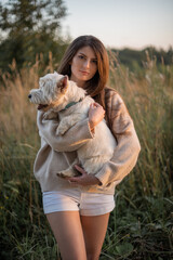 portrait of a beautiful young girl with a dog in her arms, a girl hugs her beloved petam on a walk, West Highland White Terrier,vertical portrait, copy space