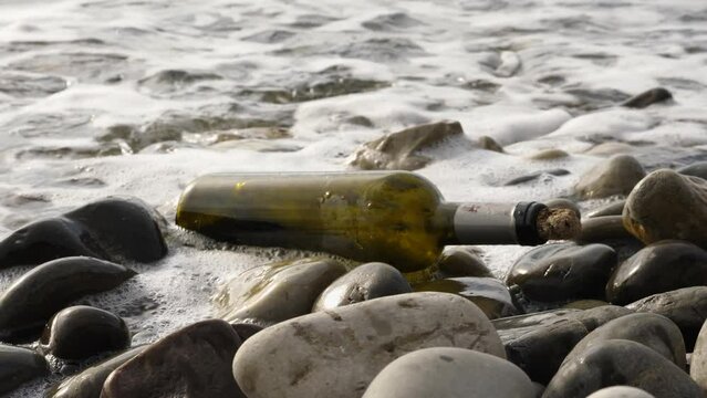 The message in the bottle on the rocks of the sea shore. An old brown bottle with the cork on it lies on the seashore. Slow motion