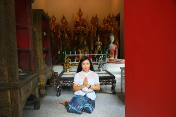 A Thai lady in Thai costume smiles and put hands together in salute at Buddhist ordination hall