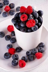 Vertical closeup shot of white plate and cup full of juicy raspberry and blueberry