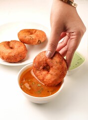 Vertical closeup of a hand dipping South Indian Medu vada in a sauce