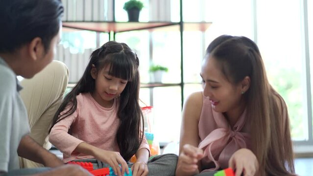 Happy Asian little girl enjoy playing a stacking blocks with her parent in living room in free time. 