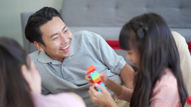 Happy Asian little girl enjoy playing a stacking blocks with her parent in living room in free time. 