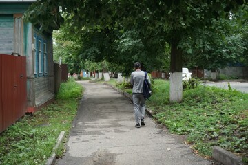 Man with a backpack from behind walking on the street with trees in the background