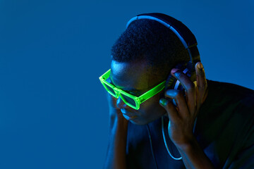 Black DJ in disco goggles checking sound in headphones in nightclub