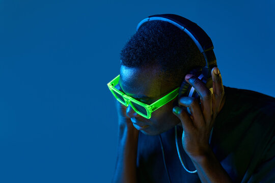 Black DJ in disco goggles checking sound in headphones in nightclub