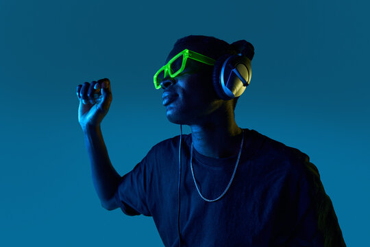 Black DJ in disco goggles checking sound in headphones in nightclub