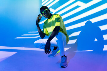Cool black man in green T shirt and sunglasses posing in shadows