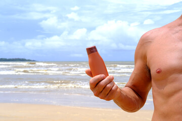 brown mockup sunscreen cream, lotion bottle in tanned male hand, sea waves in background, summer sun protection template scene with cosmetic tube on beach, product presentation, package advertisement