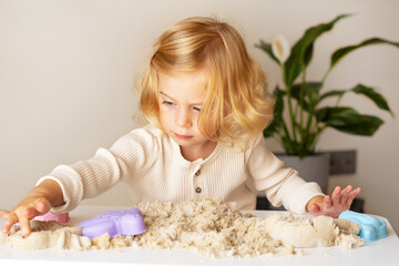 Cute happy caucasian,blonde,curly-haired toddler,baby girl playing with kinetic sand...