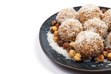 homemade coconut candies with almonds inside, sprinkled with coconut chips, lying on a round plate of dark blue color, decorated with hazelnuts isolate