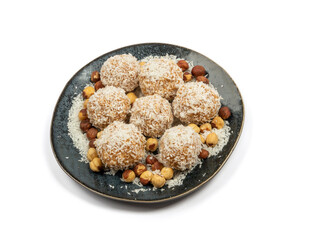 homemade coconut candies with almonds inside, sprinkled with coconut chips, lying on a round plate of dark blue color, decorated with hazelnuts isolate
