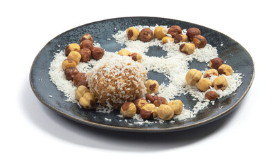 homemade coconut candies with almonds inside, sprinkled with coconut chips, lying on a round plate of dark blue color, decorated with hazelnuts isolate